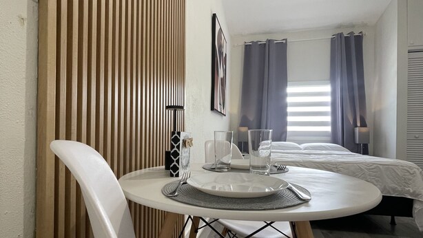 Una habitación moderna con una mesa redonda de comedor, sillas blancas, una cama y un ventilador de techo.