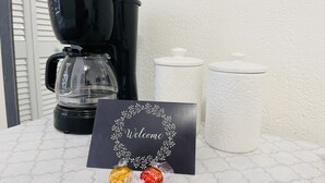 Una cafetera, un cartel de bienvenida y dos caramelos envueltos sobre una encimera.