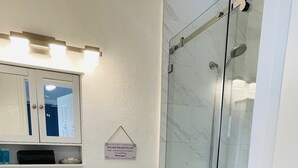 Un baño con lavamanos blanco, inodoro y ducha con mampara de vidrio.