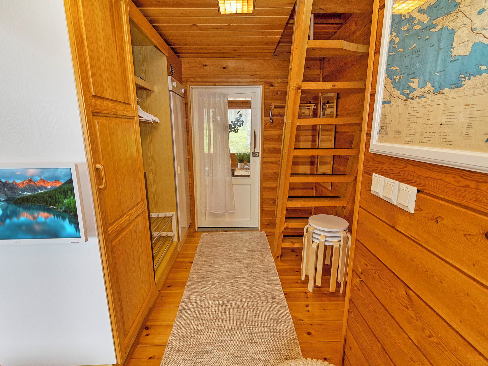 Ein hölzerner Innenbereich mit einem Gang, einer Tür zu einem Zimmer, einem kleinen Hocker und einer Karte an der Wand.