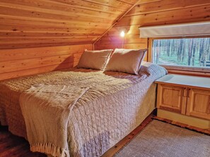 A cozy cabin bedroom with a bed, pillows, a window, and wooden walls.