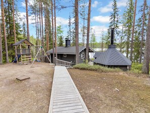 Een chalet met terras, speeltoestel en schoorsteen.