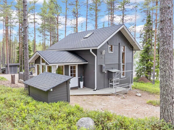 A cabin with a sloped roof, a deck, and a small shed in a forested area. - Alakitkanranta by Interhome (Kuusamo)