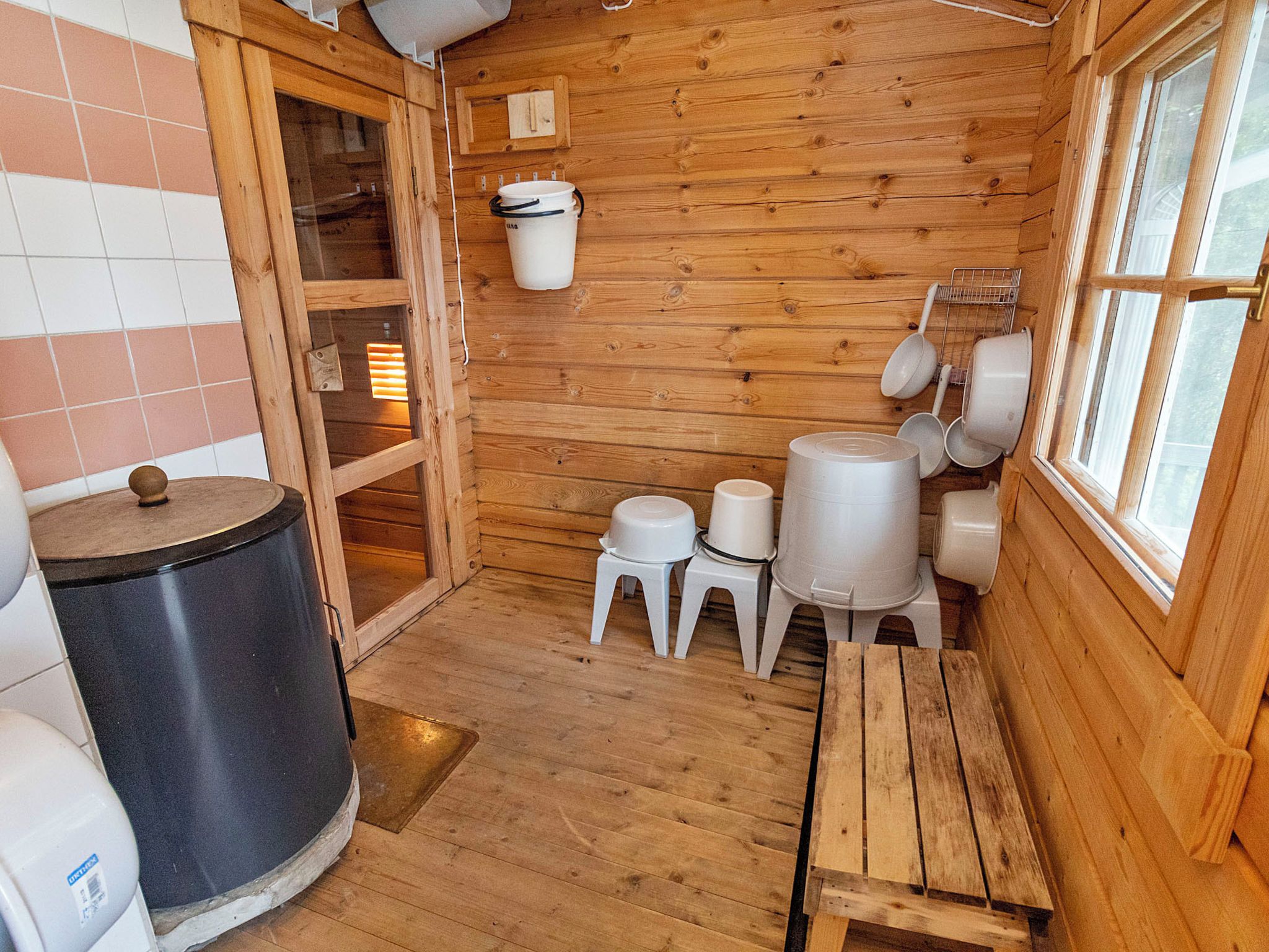 A wooden interior with a wooden bench, a trash can, and a window.