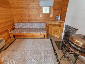Een houten blokhutinterieur met een bank, een kastje, een open haard en een vloerkleed.