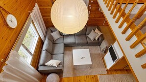 Ein modernes Interieur mit Holzbalkendecke, einem grauen Ecksofa, einem weißen Couchtisch und einer Pendelleuchte.