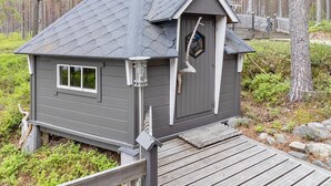 Eine Holzhütte mit steilem Dach, einer kleinen Veranda und einer Holzterrasse.