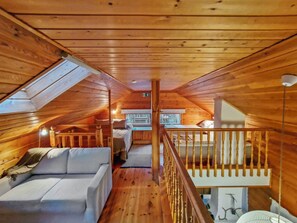 Een gezellig slaapkamer onder het dak met houten plafond, een witte bank, een klein bed en een trap naar een hoger niveau.