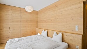 Una camera da letto moderna con una testiera in legno, un letto bianco con molti cuscini e una lampada a sospensione.