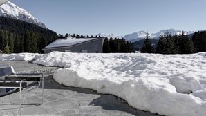 Un edificio moderno con tetto spiovente, circondato da terreno innevato e montagne sullo sfondo.