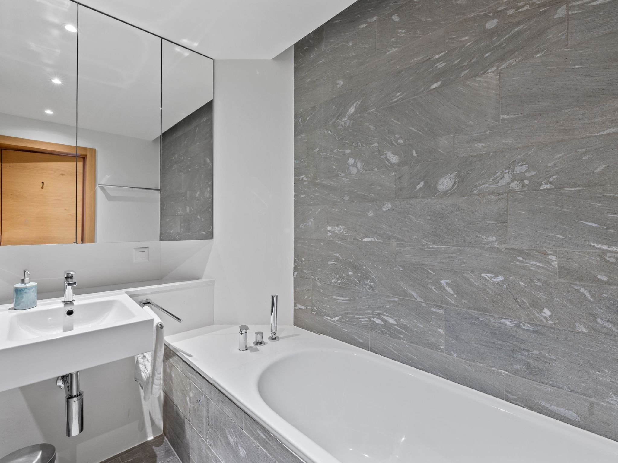Ein modernes Badezimmer mit einer großen Badewanne, einem Waschtisch inklusive Spiegel und einer Marmorwand.