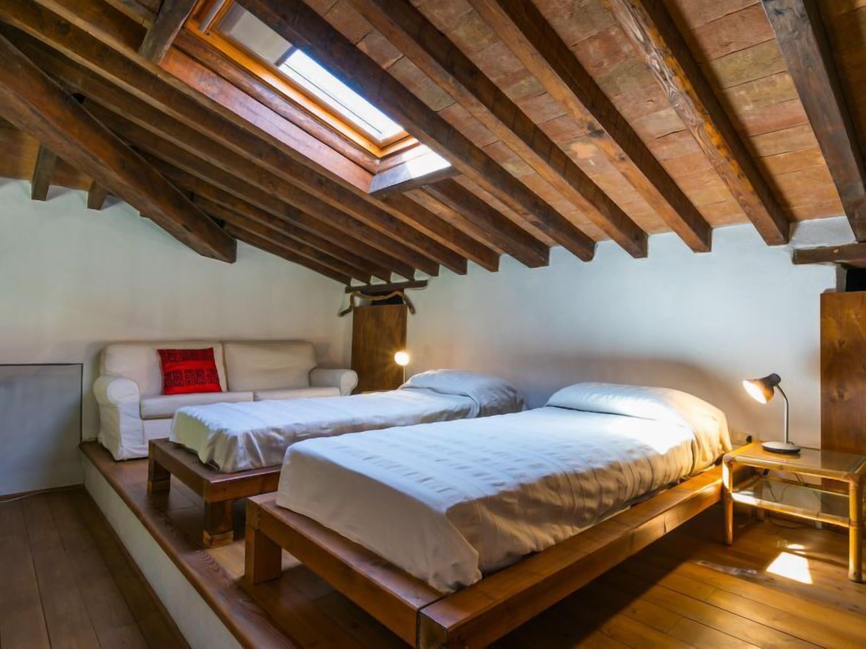 Un dormitorio estilo ático acogedor con dos camas de madera, un sofá blanco y un tragaluz.
