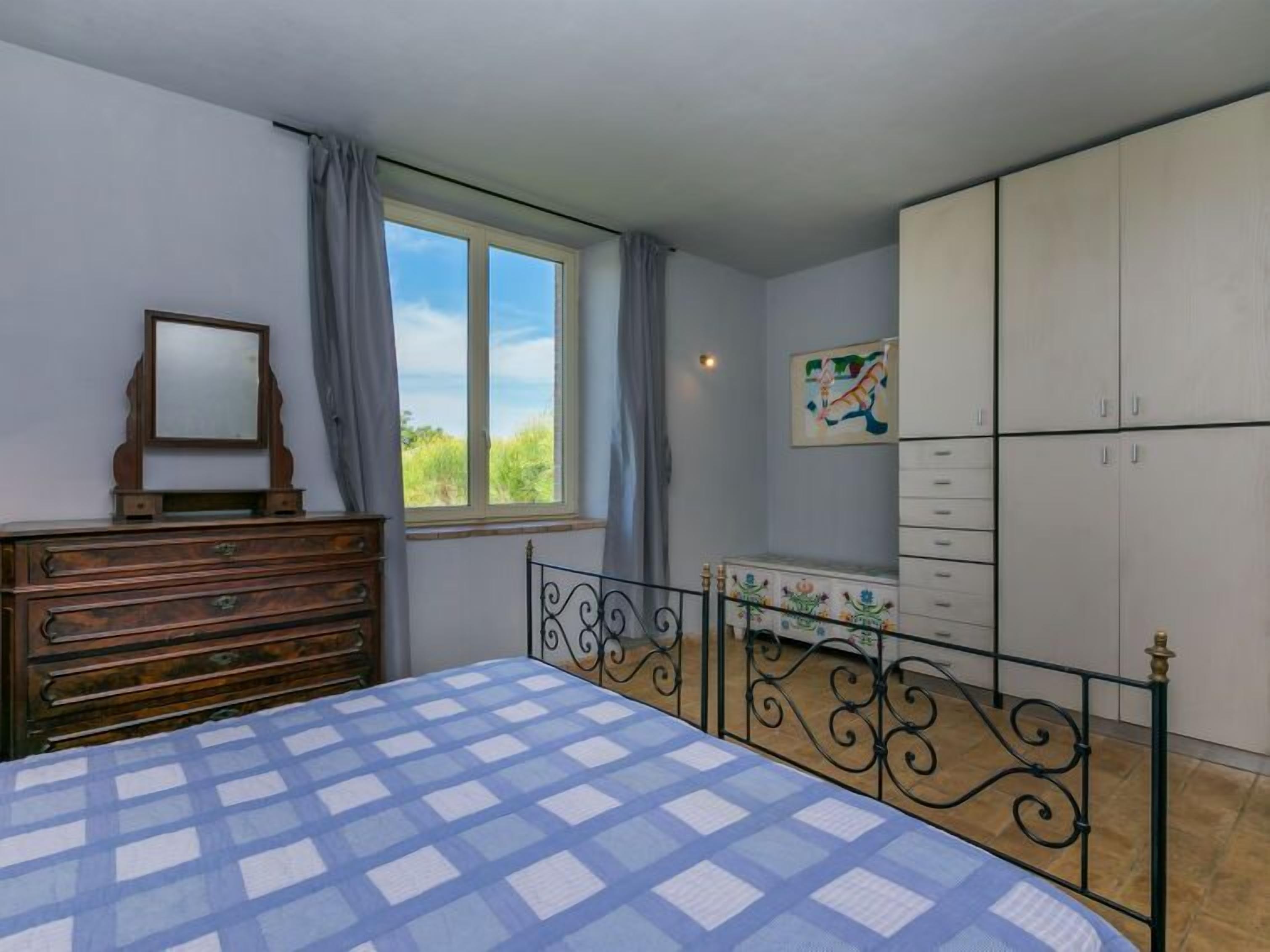 A bedroom with a bed, dresser, wardrobe, and a window with curtains.
