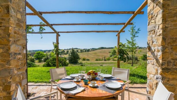 A wooden table set for four with a view of rolling hills and greenery.