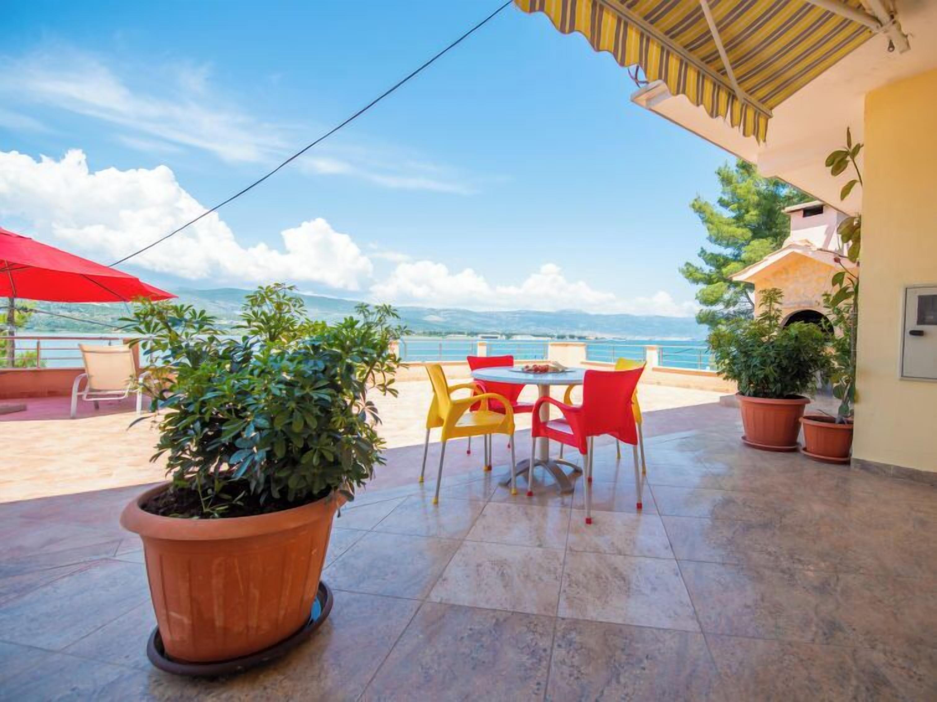 A terrace with a table and chairs, potted plants, and a view of the sea.