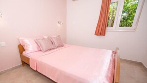 A single bed with a pink bedspread and matching pillows in a room with light pink walls and a window with a view of greenery. - Apartment Vinka by Interhome (Trogir)