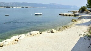 A beach with clear water, boats, and a rocky shoreline. - Apartment Vinka by Interhome (Trogir)