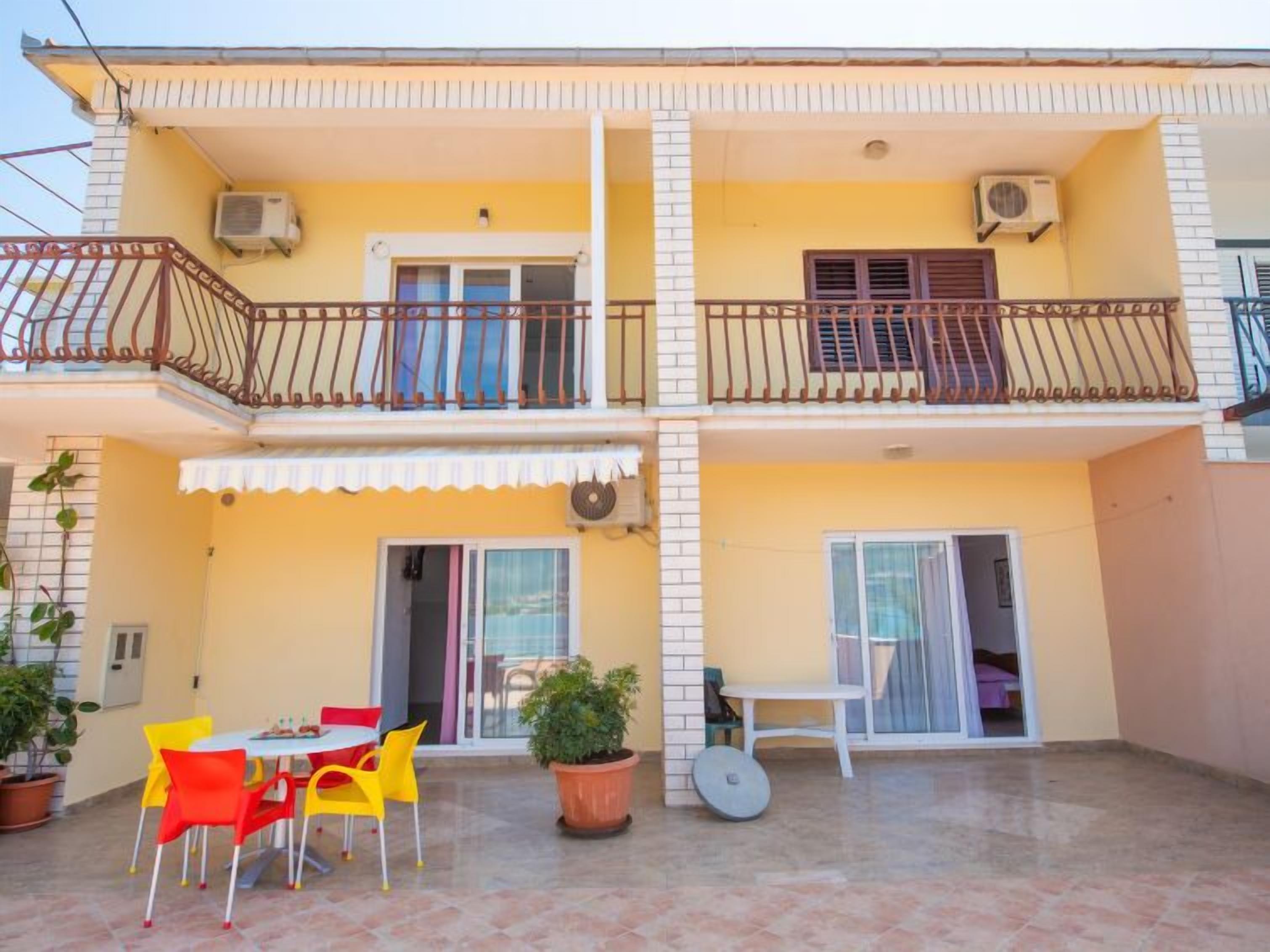 A two-story residential building with a balcony, air conditioning units, and a patio area with a table and chairs.