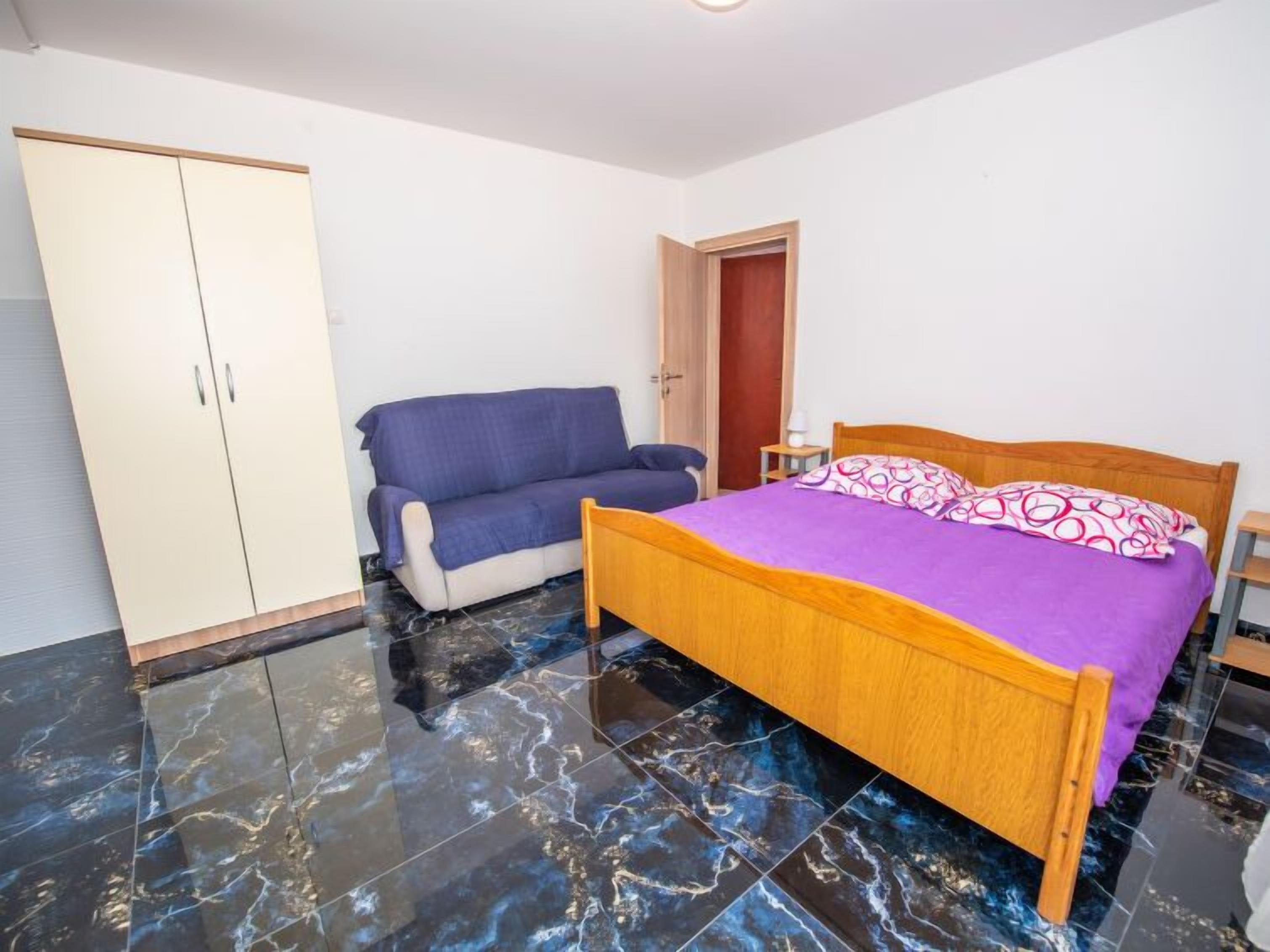 A bedroom with a bed, a wardrobe, a sofa, and a door.