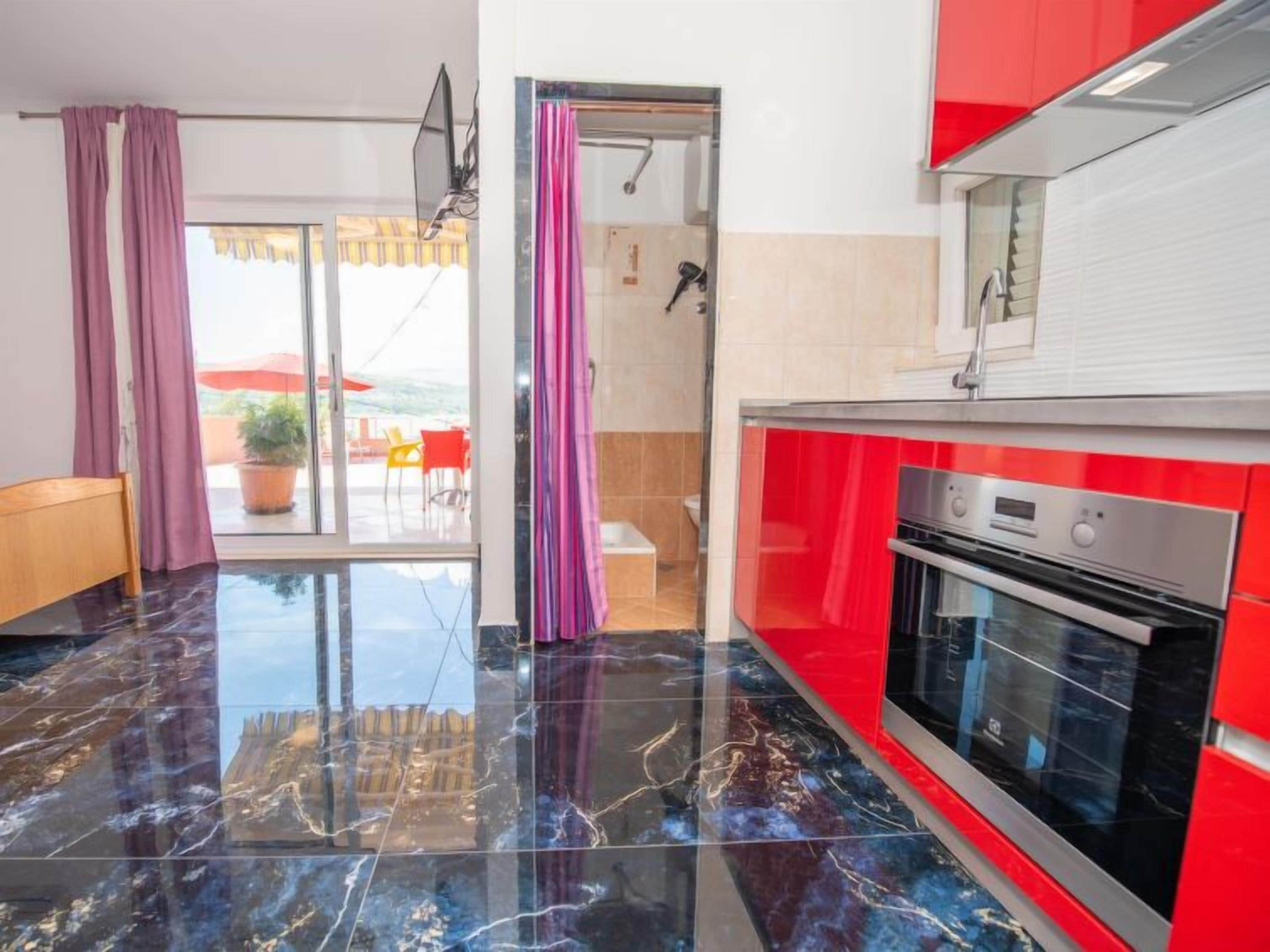 A modern kitchen with a red and white color scheme, a large oven, and a view to an outdoor seating area.