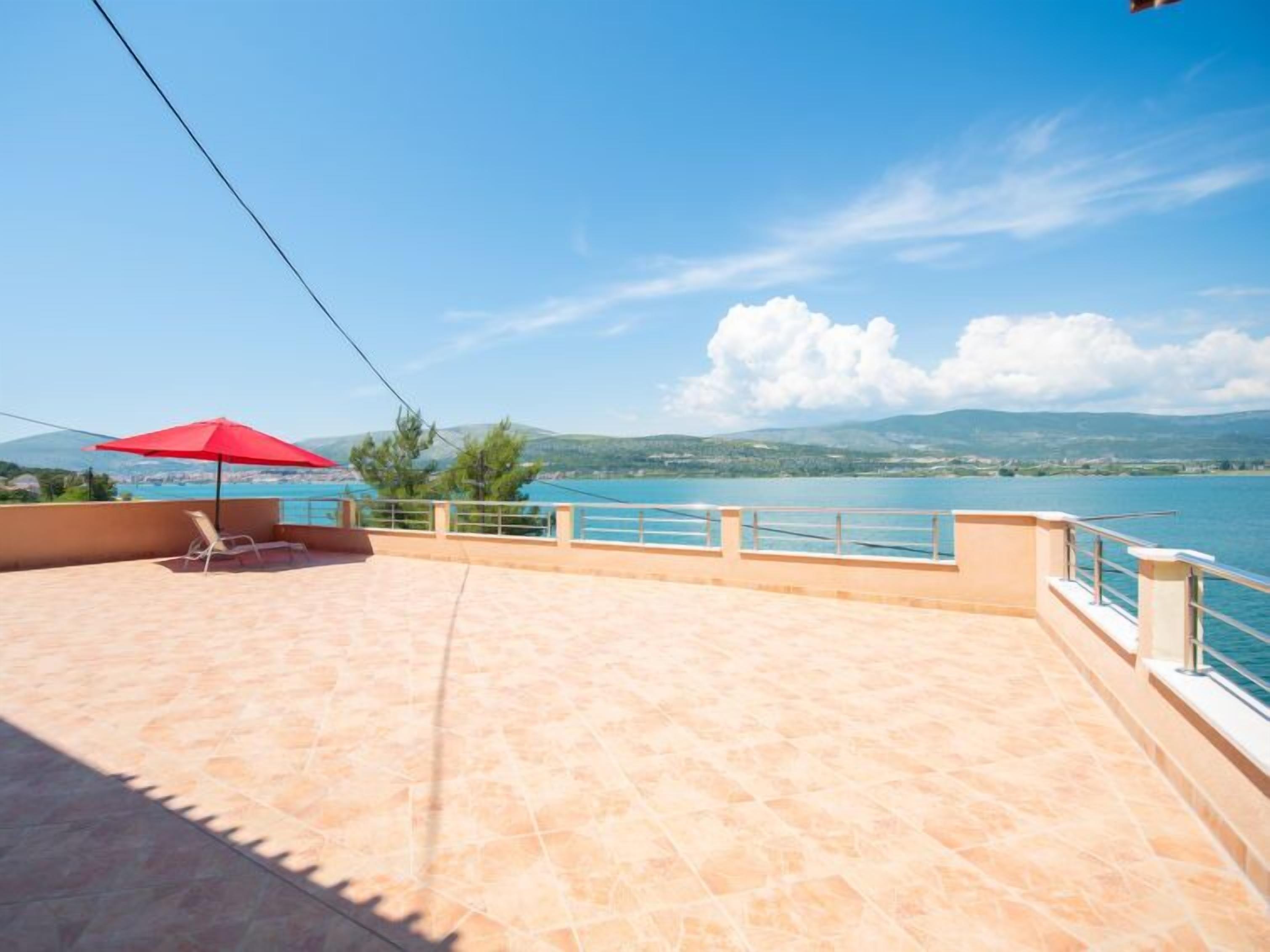 A terrace with a red umbrella, a chair, and a view of a lake and mountains.