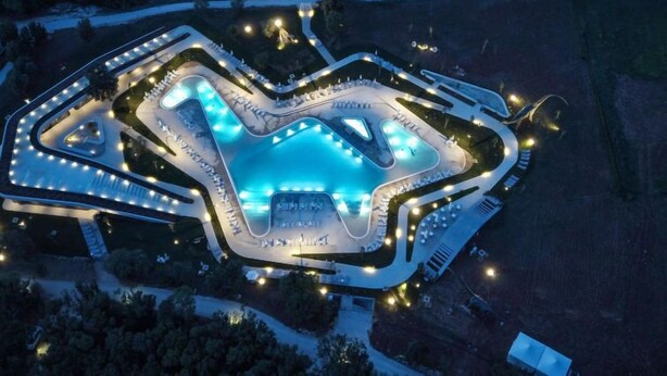 Vista aérea de un resort con un amplio área de piscina, varias habitaciones y un perímetro bien iluminado.