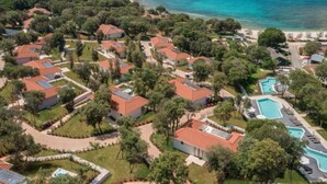 Ett flygbildsbild av ett bostadsområde vid kusten med hus, en swimmingpool och en strand.