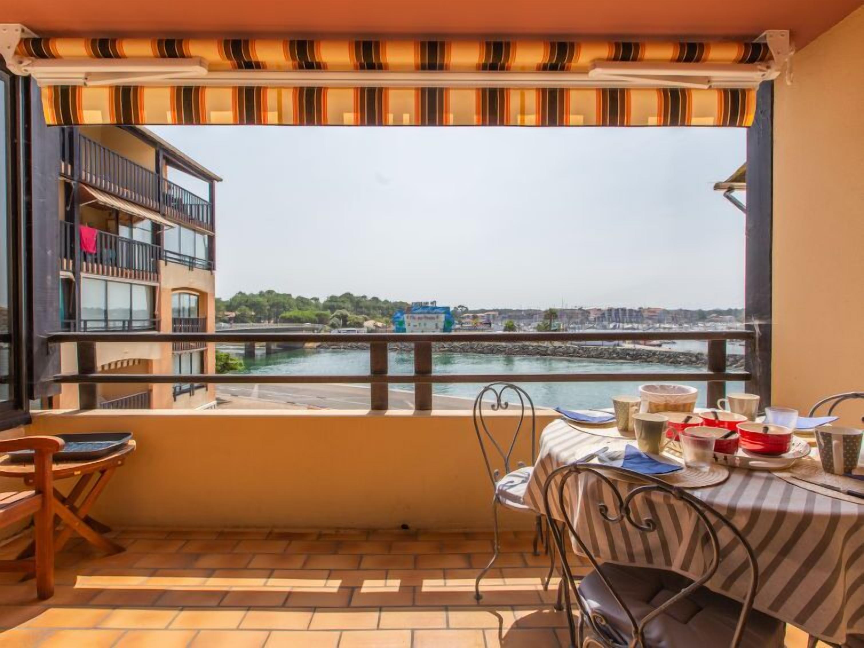 Uma varanda com vista para a orla marítima, uma mesa com cadeiras e um corrimão.