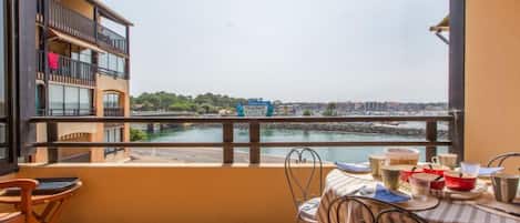 Uma varanda com vista para a orla marítima, uma mesa com cadeiras e um corrimão.