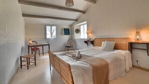 Ein Schlafzimmer mit einem großen Bett, einem Schreibtisch und einem Stuhl. Es gibt ein Fenster mit Vorhängen, eine Lampe und ein Regal mit Dekorationen.