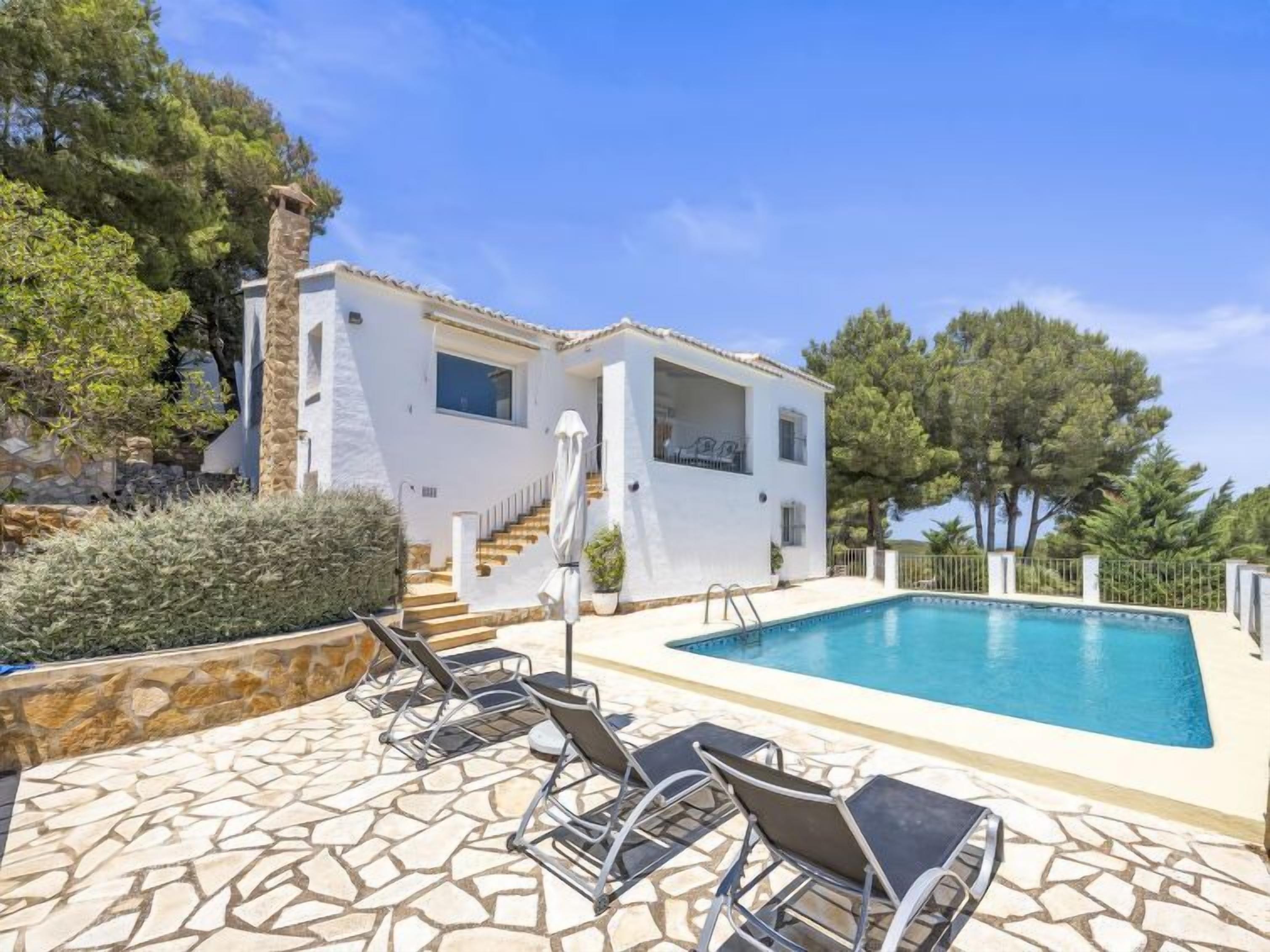 A white villa with a swimming pool, stone steps, and outdoor seating.