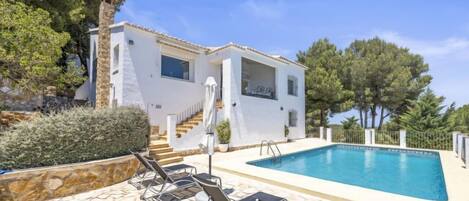 A white villa with a swimming pool, stone steps, and outdoor seating.