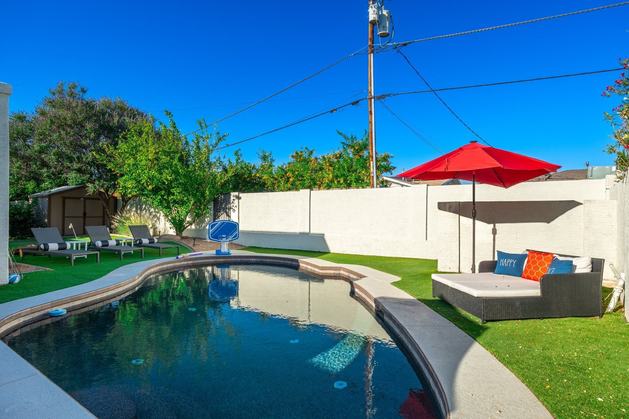 Un jardin avec une piscine, un parasol rouge et un coin salon agrémenté de coussins.