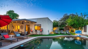 A modern outdoor pool area with lounge chairs, a dining table, and a covered patio.