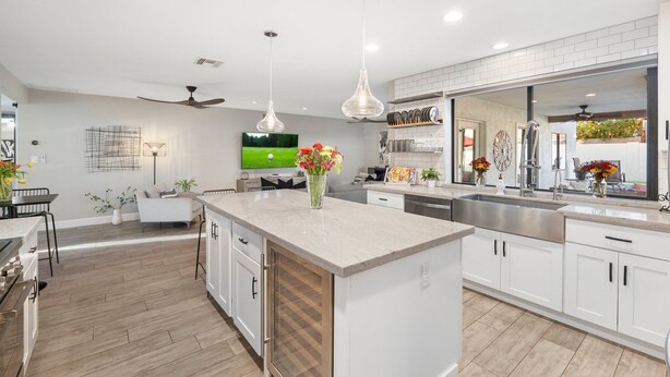A modern kitchen with white cabinetry, a large island, pendant lighting, and a TV on the wall.