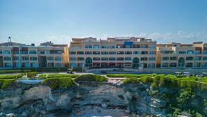 A hotel with multiple floors, a central courtyard, and a rocky shoreline with waves. - Caribbean Views. 2 BR at Isla 33. Rooftop Pool. (Isla Mujeres)