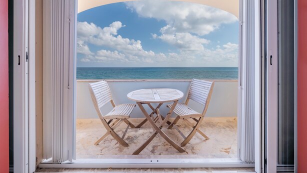 A balcony with a table and chairs, overlooking a beach and the sea. - Caribbean Views. 2 BR at Isla 33. Rooftop Pool. (Isla Mujeres)