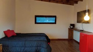 A bedroom with a bed, a TV mounted on the wall, a small kitchenette, and a red cabinet. - Kleines Landhaus in 25 Ha in den Bergen von Córdoba, im Herz Argentiniens (Villa Berna)