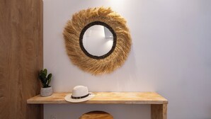 A wooden console table with a round mirror, a white hat, and a potted plant. - Sand Gem - Beach Apartments (Santorini)