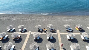 A beach with rows of sun loungers and thatched umbrellas, arranged in a grid pattern. - Sand Gem - Beach Apartments (Santorini)