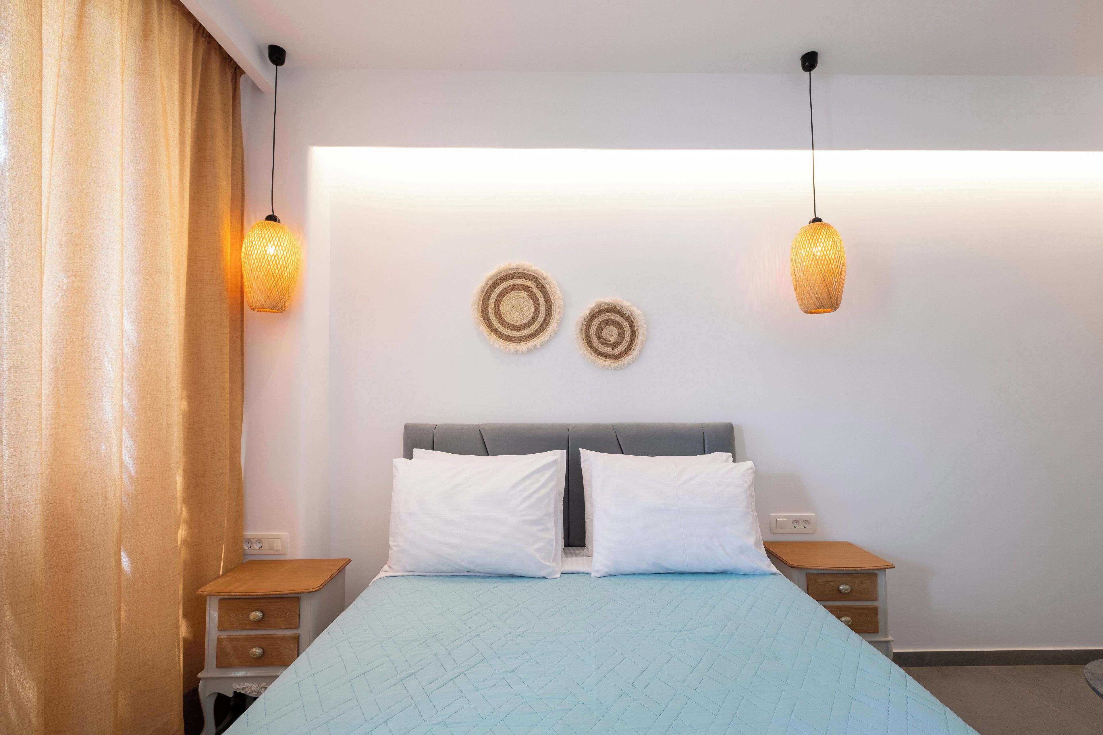 Un dormitorio con una cama, dos mesitas de noche, una lámpara de pared y una cortina.