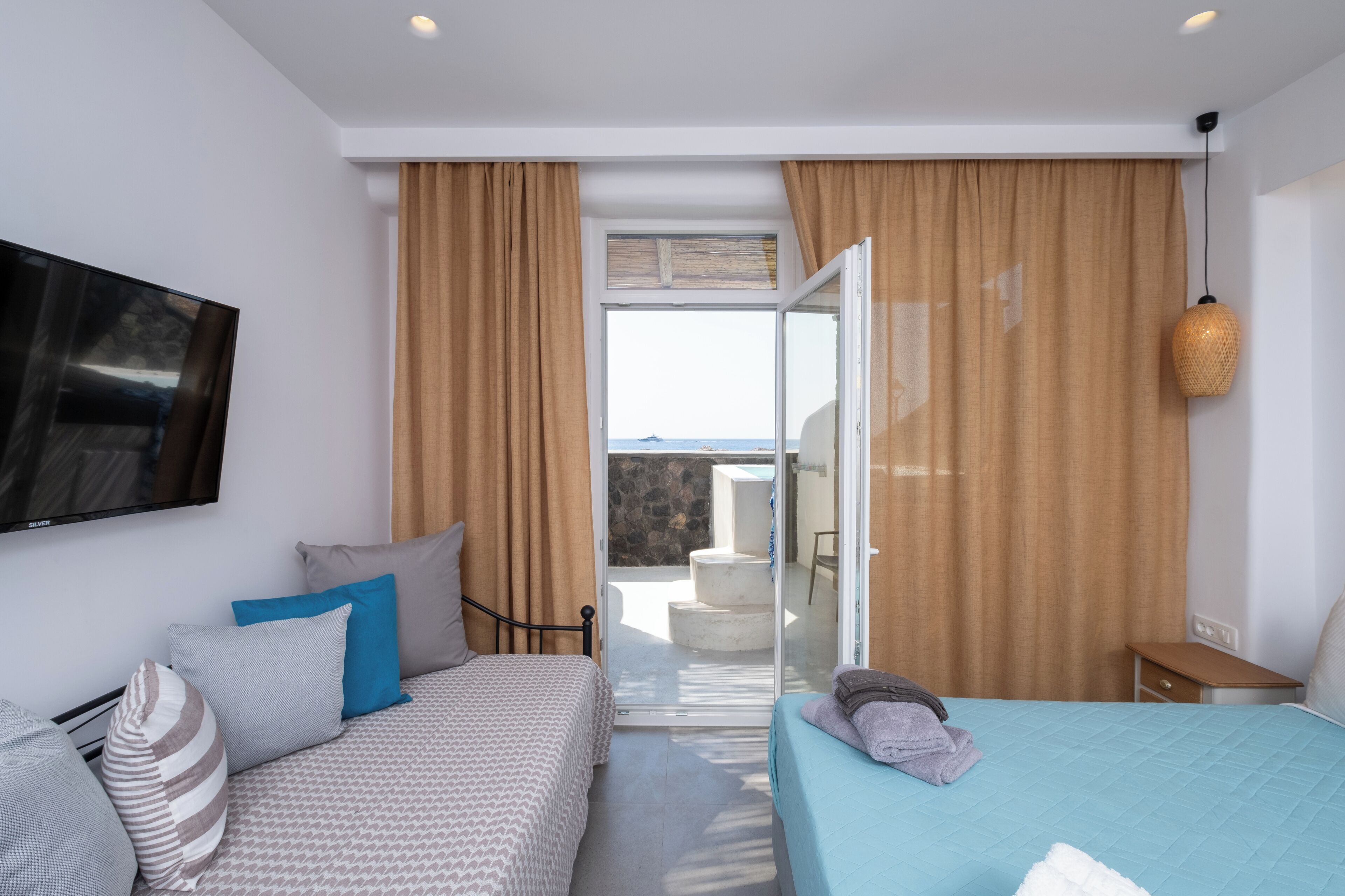 Un dormitorio con cama, televisión, balcón con vistas y puerta corredera.