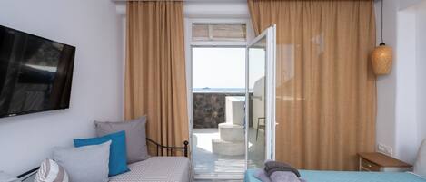 Un dormitorio con cama, televisión, balcón con vistas y puerta corredera.