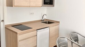 A compact kitchen with wooden cabinets, a built-in microwave, a dishwasher, and a small dining area with metal chairs. - Casa en El Palmar de Vejer a 200 Metros de la Playa (El Palmar de Vejer)