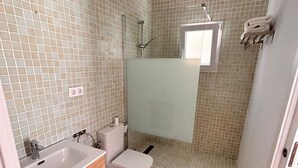 A bathroom with a tiled shower, a toilet, and a sink with a wooden vanity. - Casa en El Palmar de Vejer a 200 Metros de la Playa (El Palmar de Vejer)