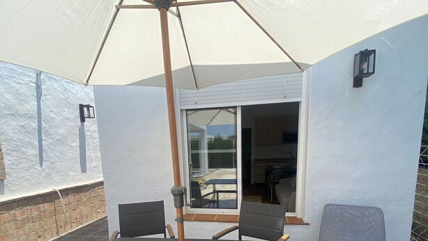 An outdoor patio with a table and chairs under a large umbrella, a glass door leading to an interior space, and a brick wall. - Casa en El Palmar de Vejer a 200 Metros de la Playa (El Palmar de Vejer)
