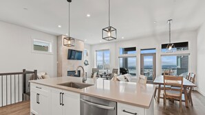 Une cuisine moderne dotée d’un grand îlot central, d’appareils électroménagers en acier inoxydable et d’un coin repas avec des chaises et une table en bois.