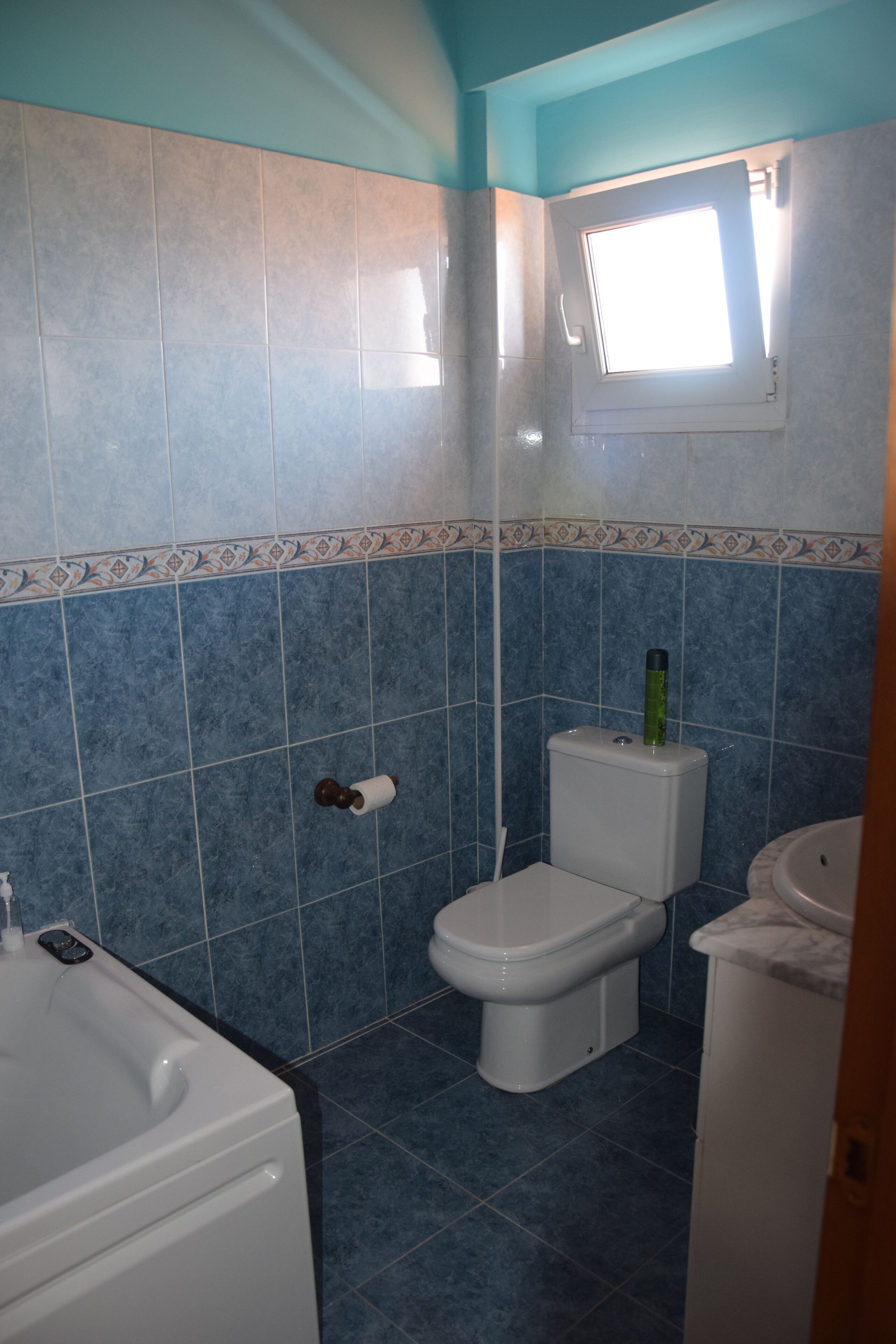 Une salle de bain avec des carreaux bleus, des toilettes, un lavabo et une fenêtre.