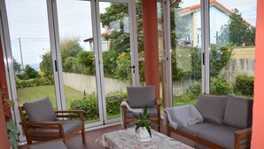 Eine sonnendurchflutete Terrasse mit einem Holztisch, zwei Stühlen und einer Couch.