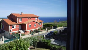 Ein rotes, zweistöckiges Haus mit rotem Ziegeldach, einem grünen Zaun und Blick aufs Meer.